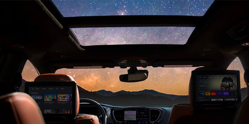 The interior of a vehicle at night, showing the sunroof and infotainment screens