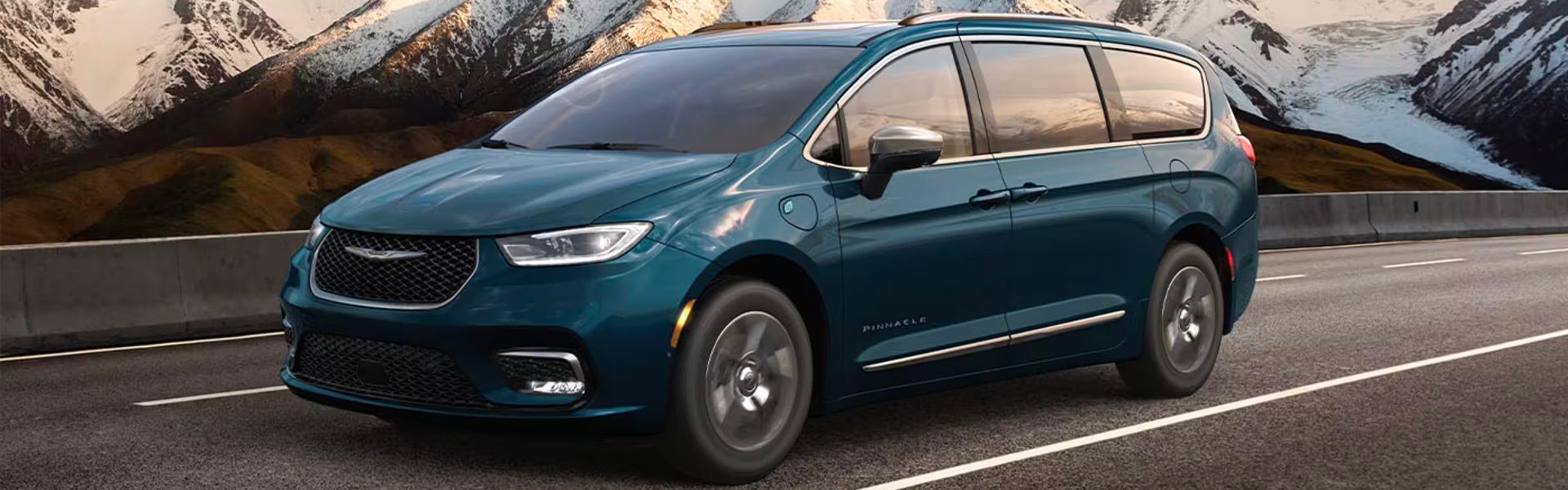 A teal Chrysler Pacifica minivan driving on a highway with snow-capped mountains in the background