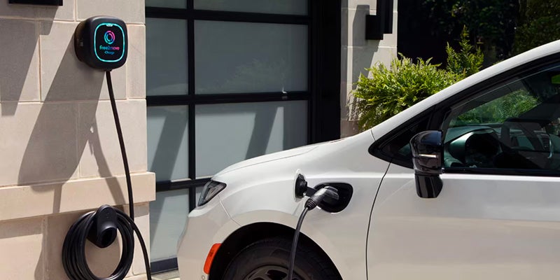White minivan plugged into a wall-mounted electric charger at home