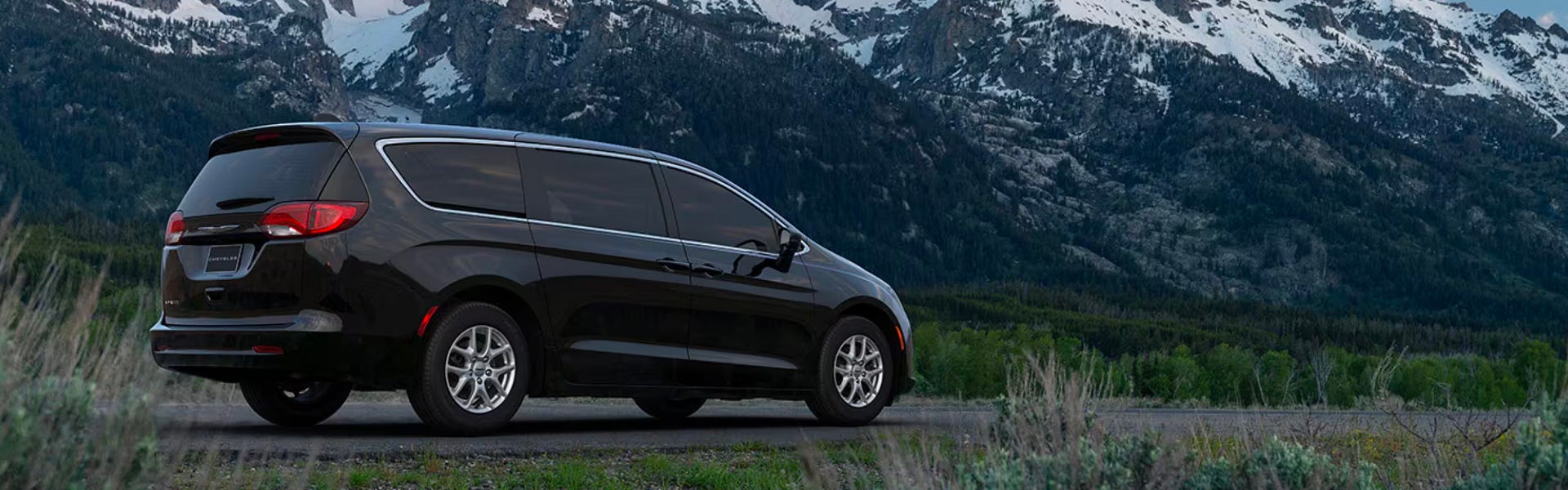 Rear three-quarter view of a black Chrysler minivan parked near snowy mountains