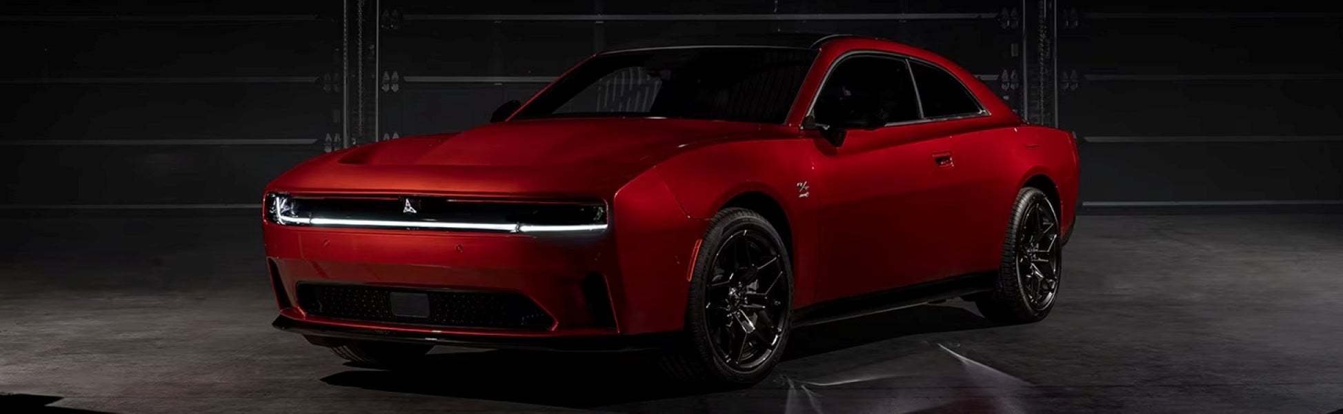 A front three-quarter view of a red Dodge Charger coupe with black wheels in a dark studio