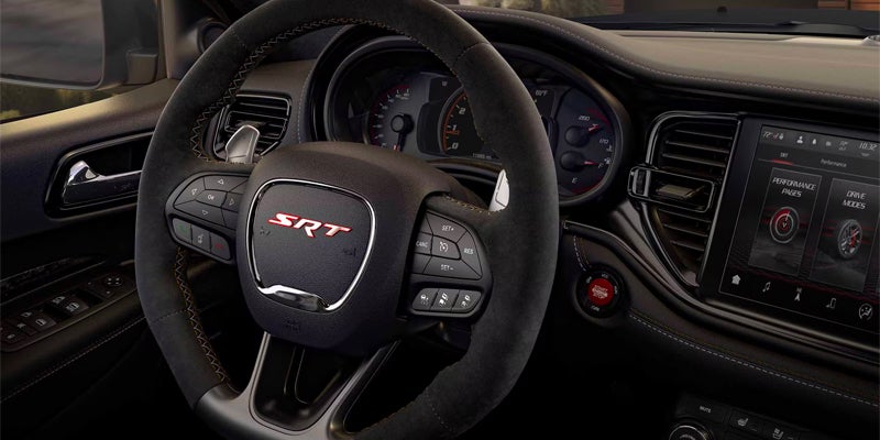 The interior of a vehicle, showing the steering wheel with a red "SRT" logo, and the dashboard