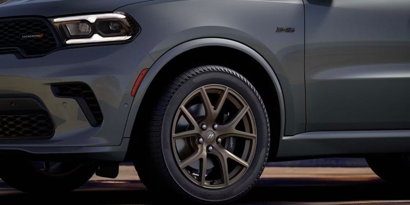 The front quarter panel of a dark green Dodge Durango with its black wheel