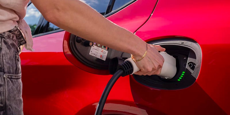 Hand plugging an electric charger into a red Dodge Hornet