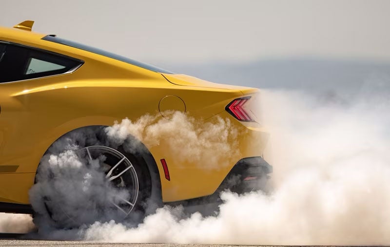 Yellow sports car doing a burnout with smoke around the rear tire.