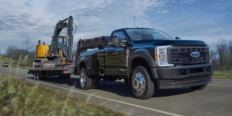 A black Ford Super Duty truck towing an excavator.