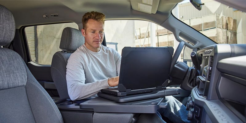 A man using a laptop in the front seat of a Ford Super Duty