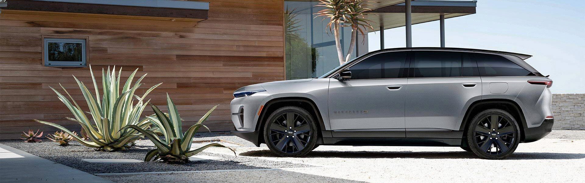 A silver Jeep Wagoneer S electric SUV parked outside a modern wood-paneled house with desert plants