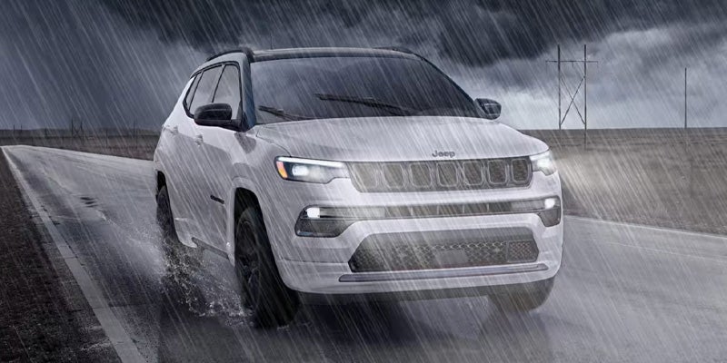 White Jeep Compass driving in heavy rain on a wet road