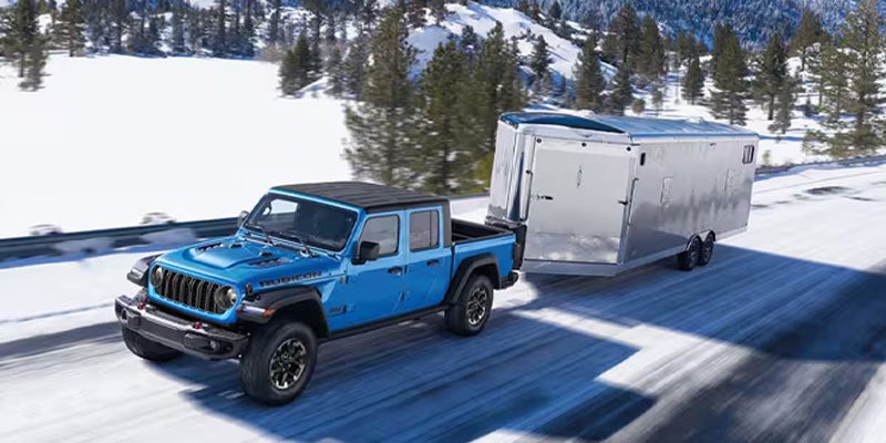 Blue Jeep Gladiator towing a silver enclosed trailer on a snowy road
