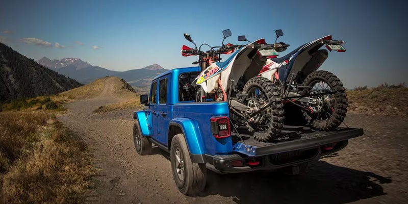Blue Jeep Gladiator carrying two motorcycles in its bed on a mountain trail