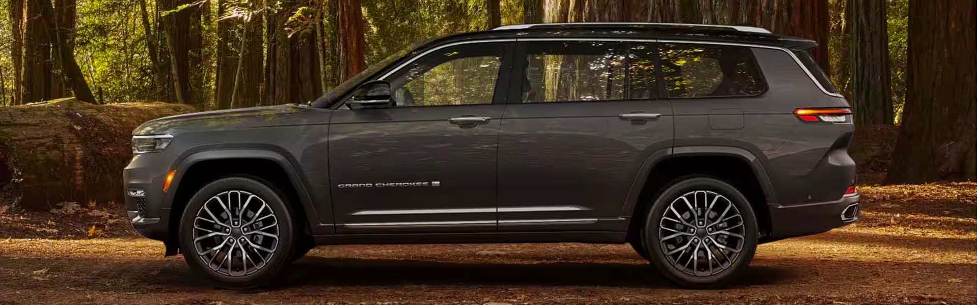 Side view of a dark gray Jeep Grand Cherokee L SUV parked in a forest.