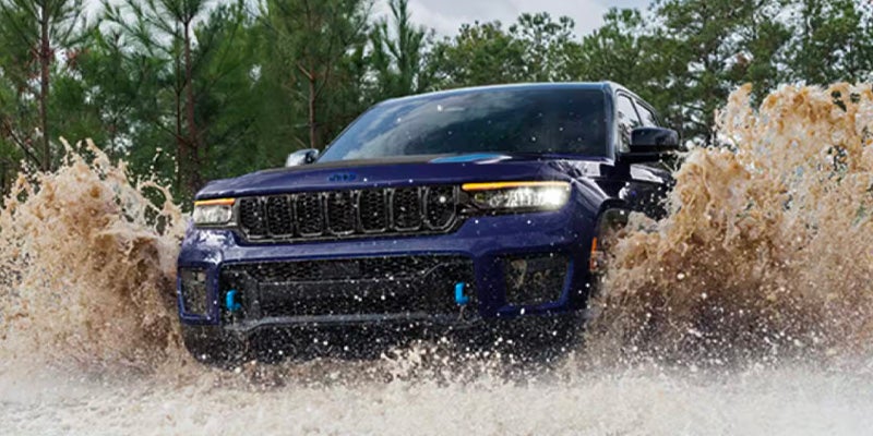 A blue Jeep Grand Cherokee L driving through a muddy puddle