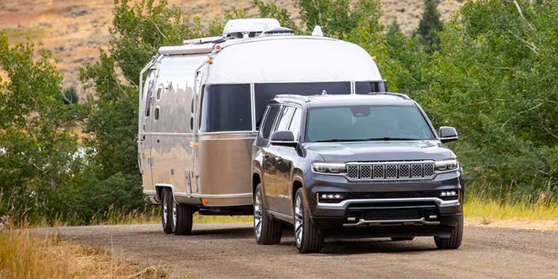 A black Jeep Grand Wagoneer tows a silver Airstream trailer on a dirt road