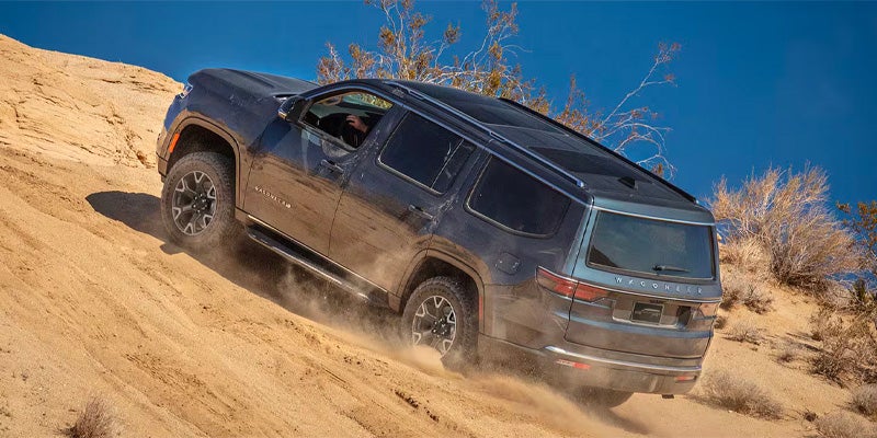 Large SUV driving up a steep, sandy hill in a desert environment
