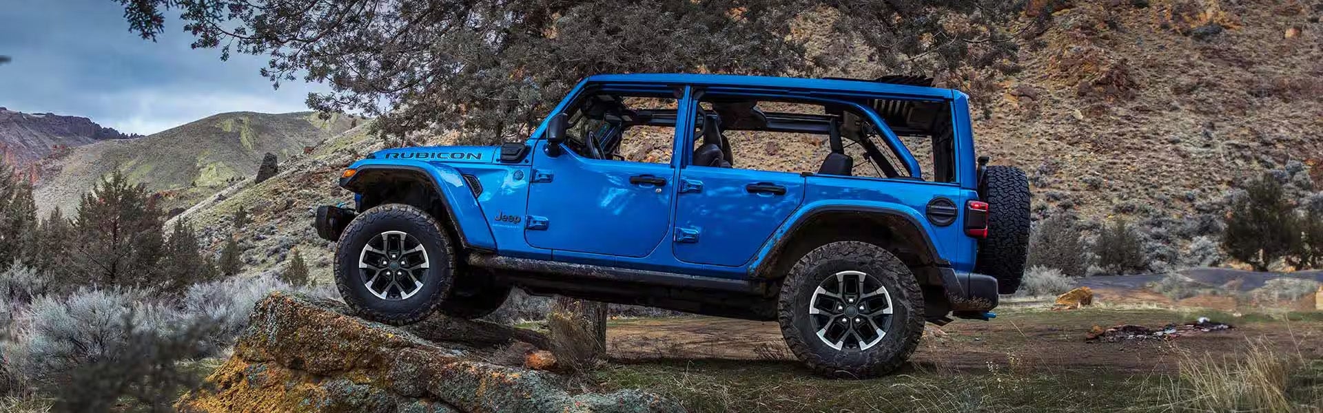 A vibrant blue Jeep Rubicon is off-roading on a rocky terrain.