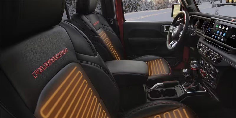 The black leather interior of a Jeep Rubicon features heated seats with orange stitching.