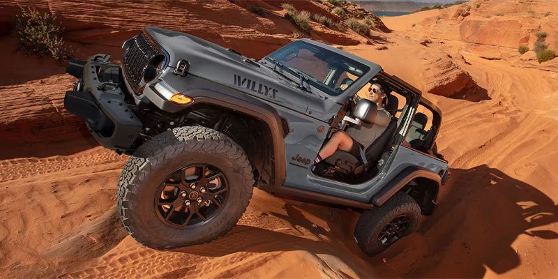 A gray Jeep Wrangler Willys is off-roading on a sand dune
