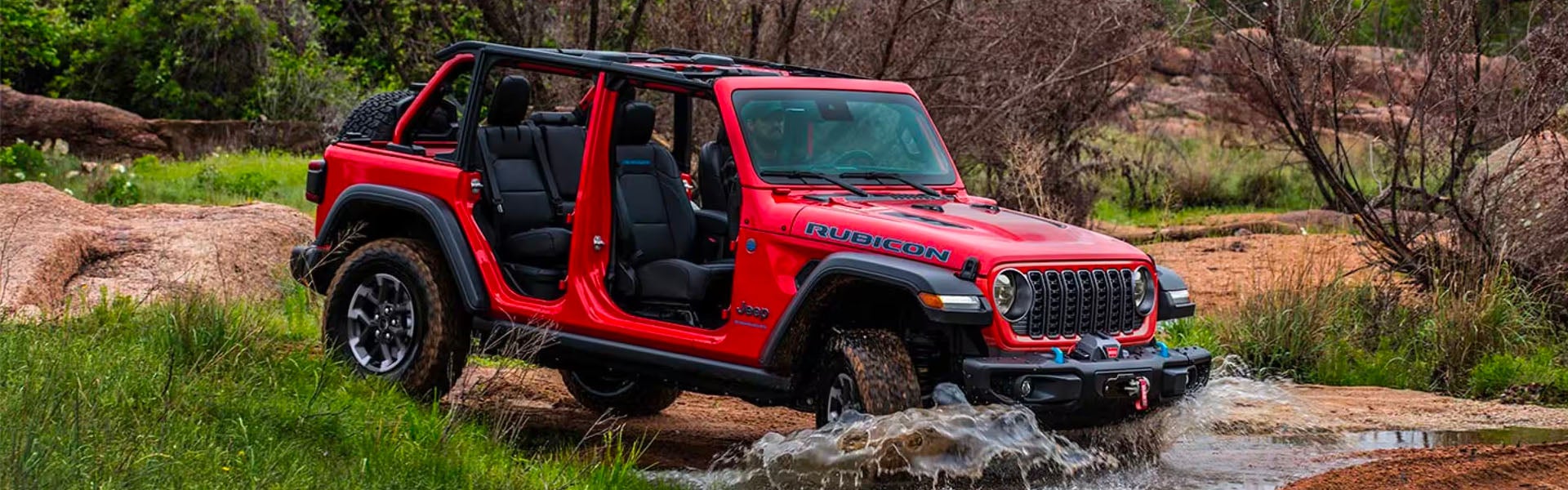 A red Jeep Wrangler Rubicon 4-door, with doors and roof removed, drives through water