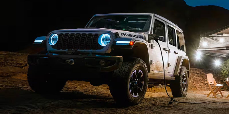Front view of a white Jeep Wrangler parked at night with headlights on