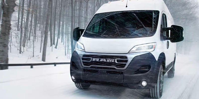 A white Ram ProMaster van driving in a snowy forest.